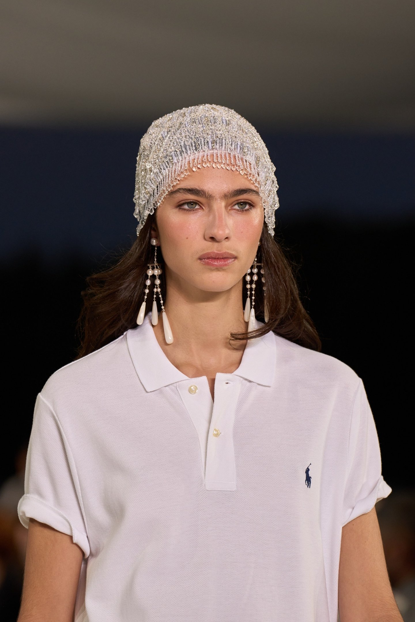 Modelo usa brincos longos com pérolas e pingentes, destacando tendências de acessórios elegantes na moda.