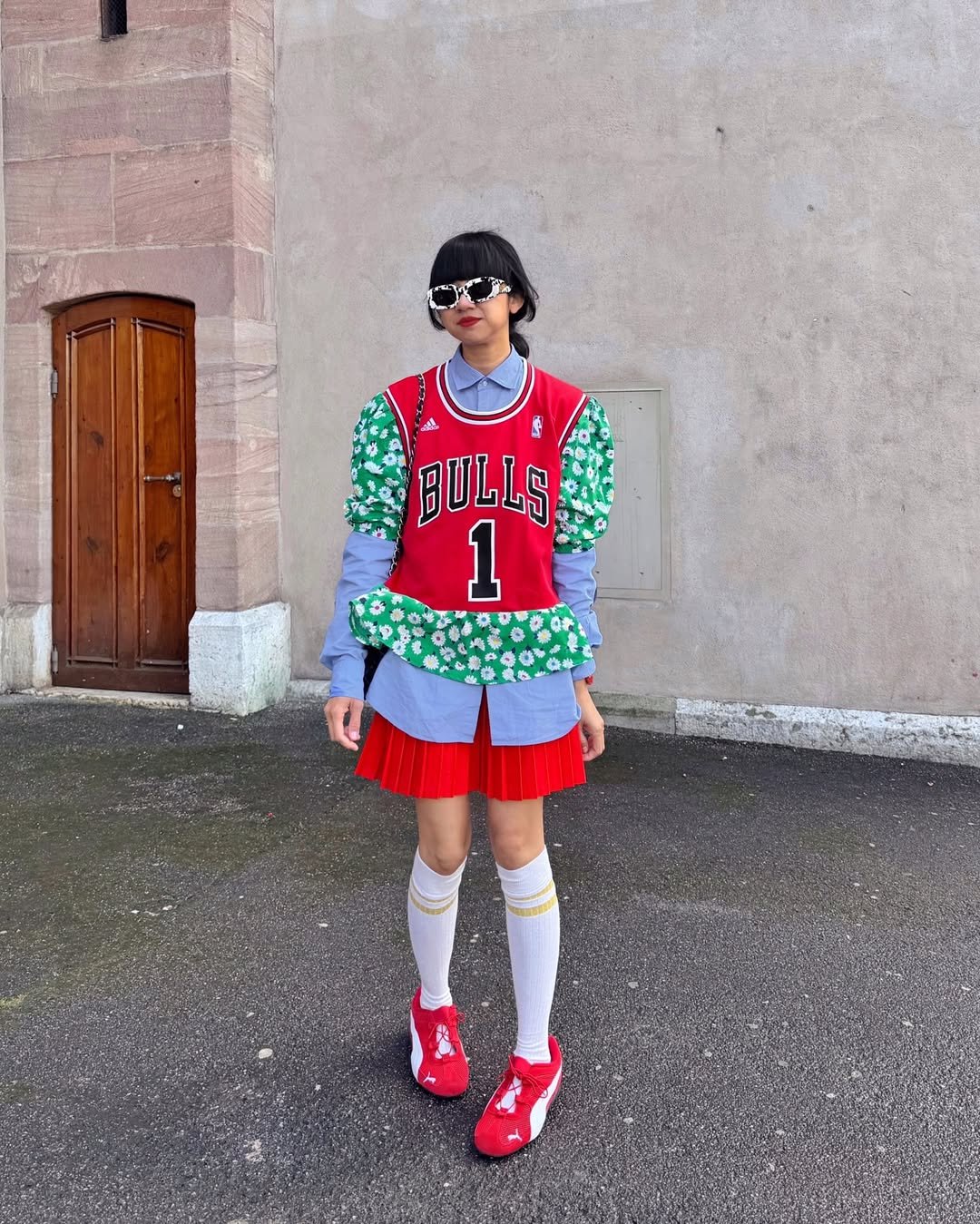 Pessoa usando camiseta de basquete, blusa estampada, saia vermelha, meias brancas e tênis vermelhos.