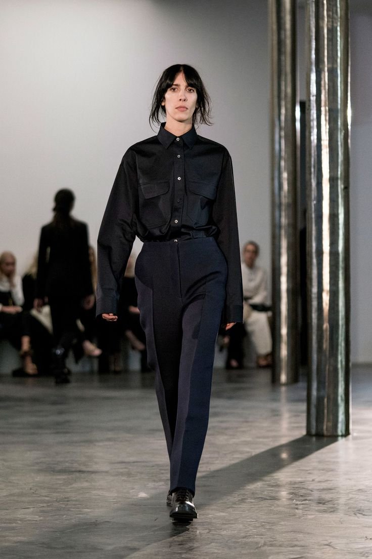 Modelo desfilando com terninho preto em ambiente elegante e minimalista.