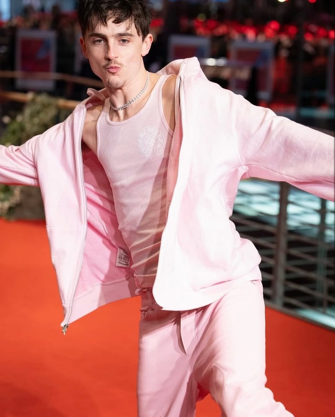 Homem usando roupas rosas, incluindo jaqueta e regata, estilo inspirado na moda Y2K em um tapete vermelho.