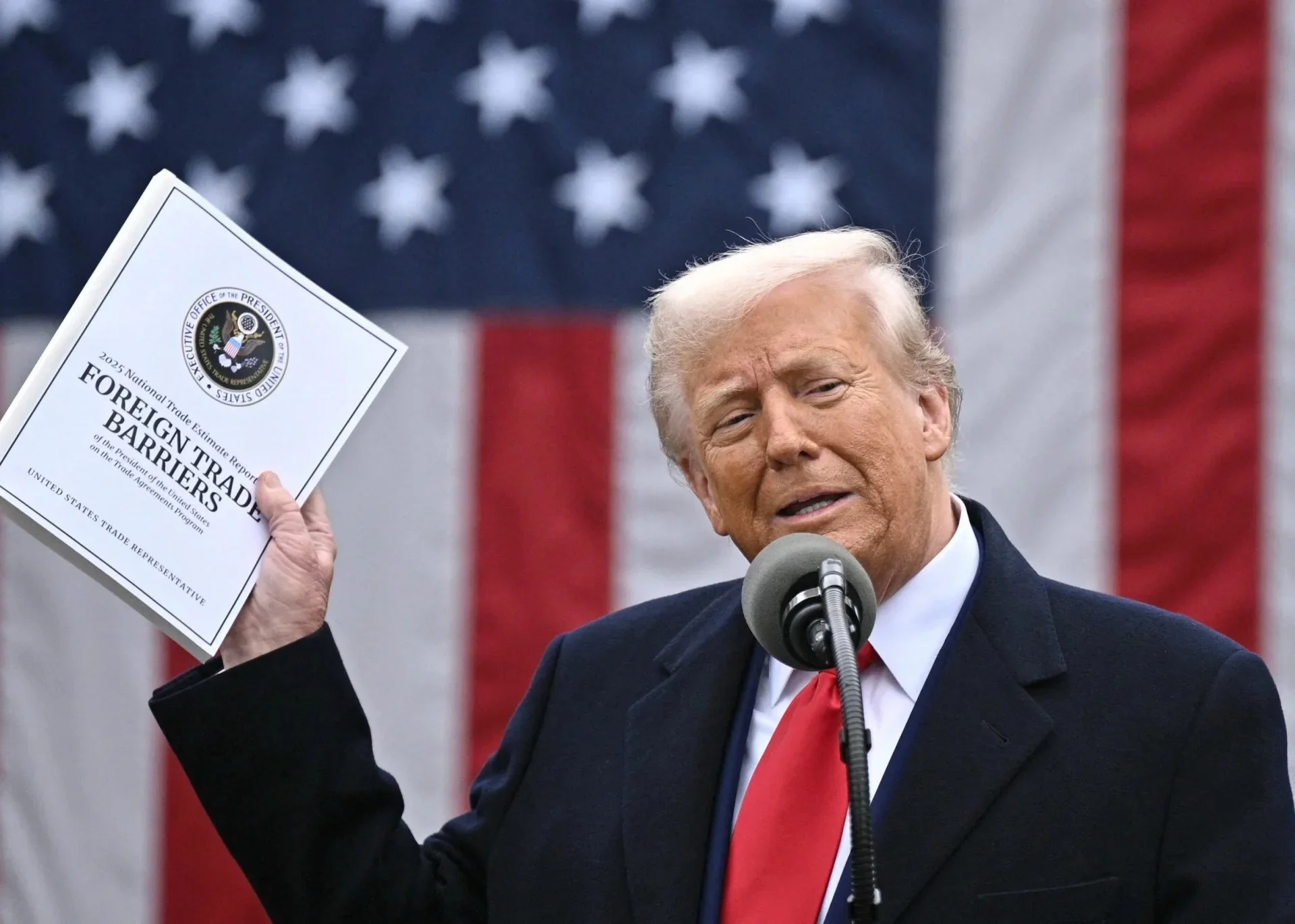 Homem segurando relatório de barreiras comerciais com bandeira dos EUA ao fundo. Taxas do trump