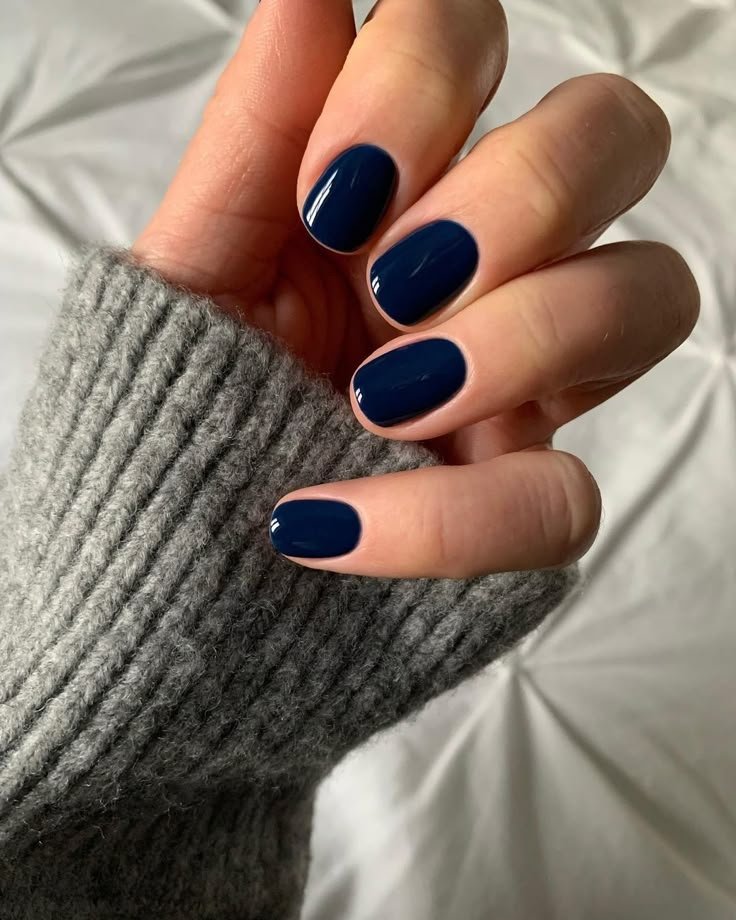 Unhas pintadas de azul escuro, combinando com um suéter cinza, ideal para unhas de inverno.
