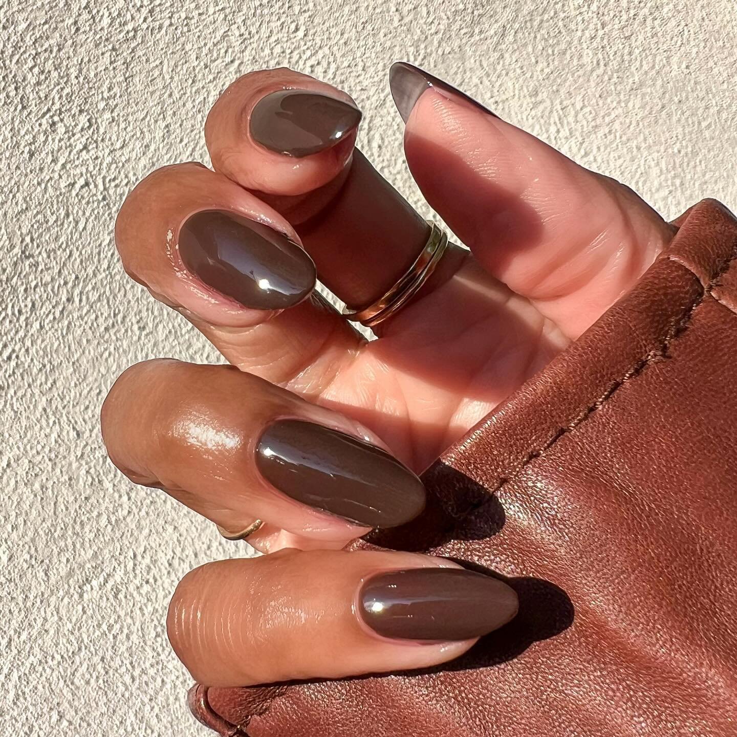 Mãos com esmalte marrom escuro, semelhante a unhas de inverno, segurando uma jaqueta de couro marrom.