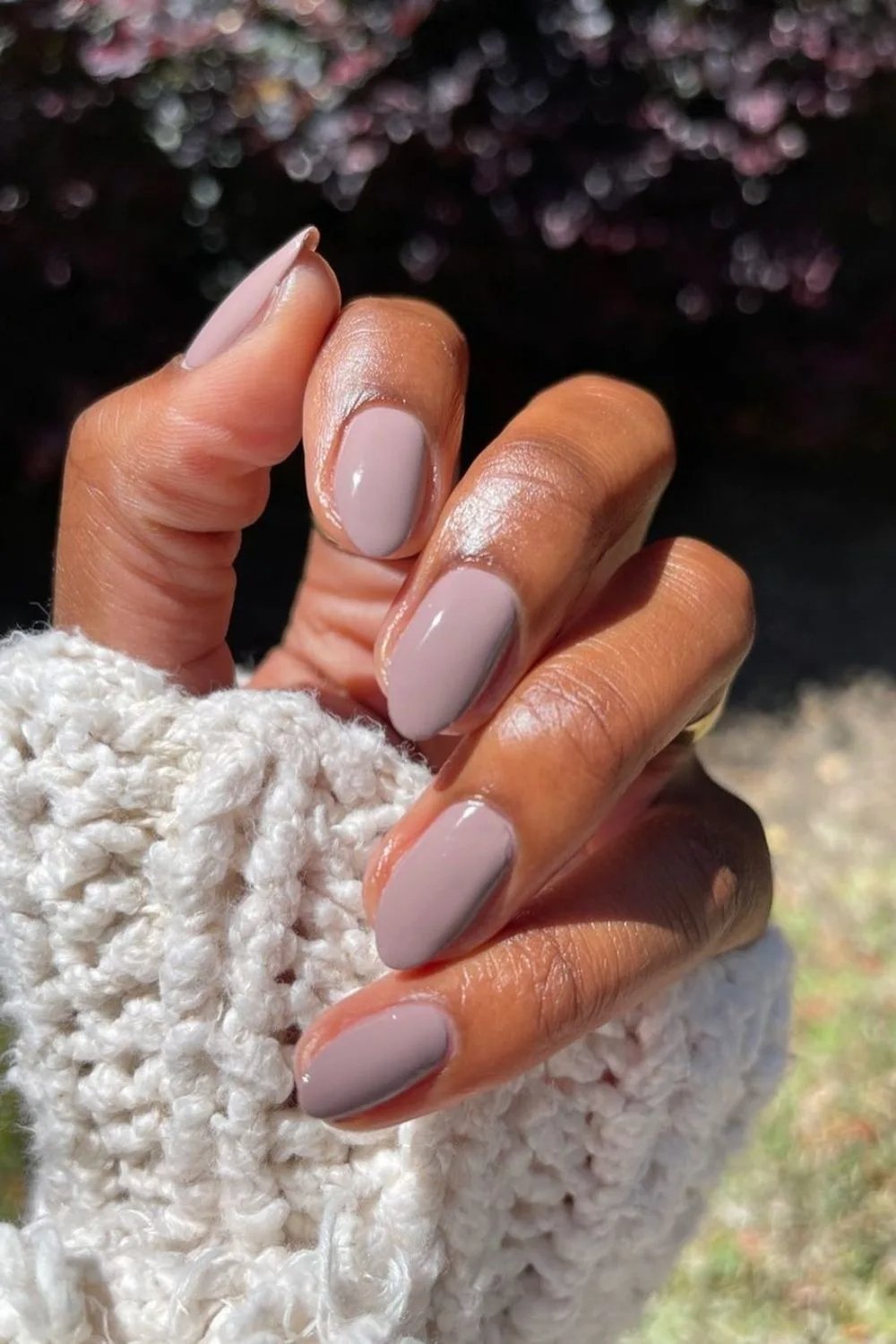 Unhas em tom nude combinam com suéter de malha branca, estilo unhas de inverno.
