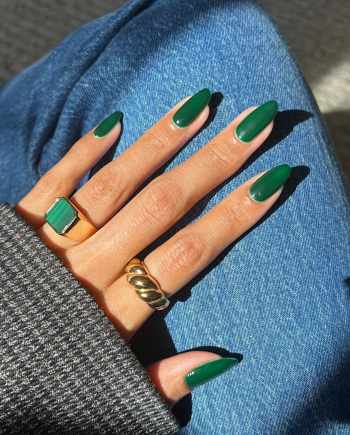 Unhas verdes escuras em mão sobre calça jeans, criando um visual de inverno elegante.