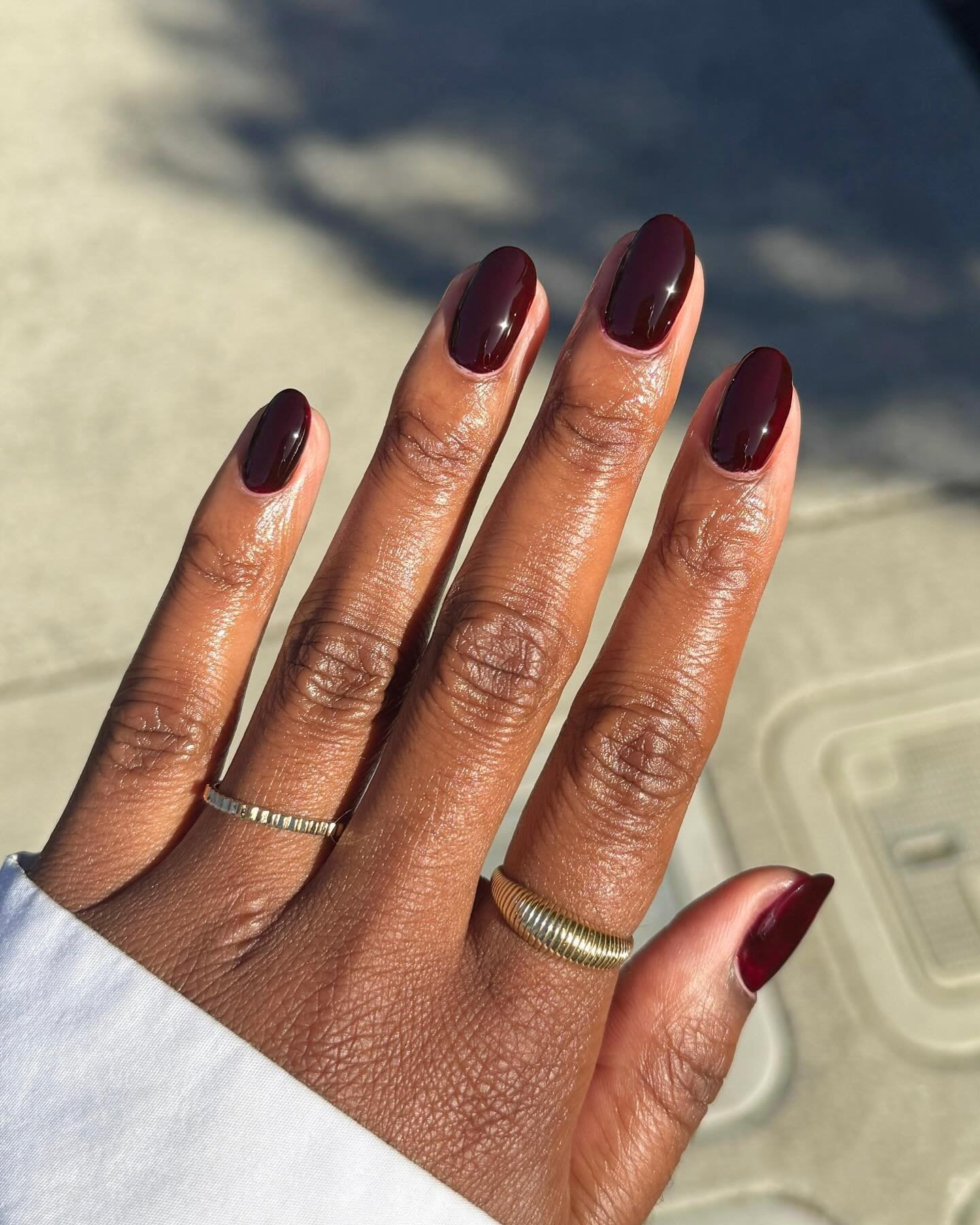 Unhas esmaltadas em tom vinho com anéis dourados, refletindo o estilo de unhas de outono.