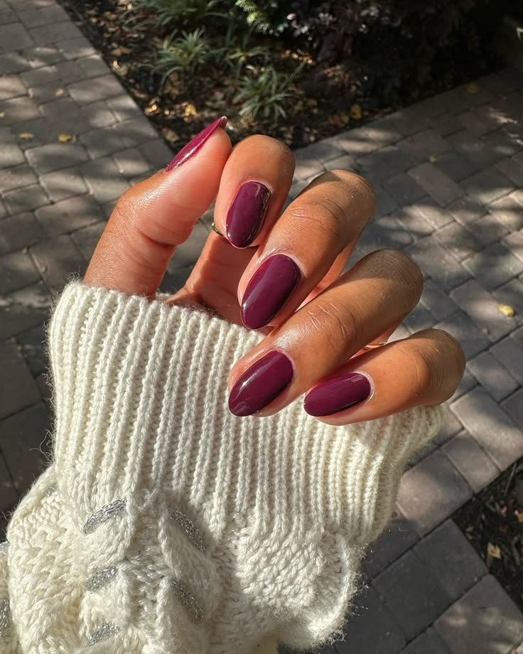 Unhas pintadas de vermelho-escuro, refletindo uma paleta de outono, adornam uma mão com suéter branco de tricô.