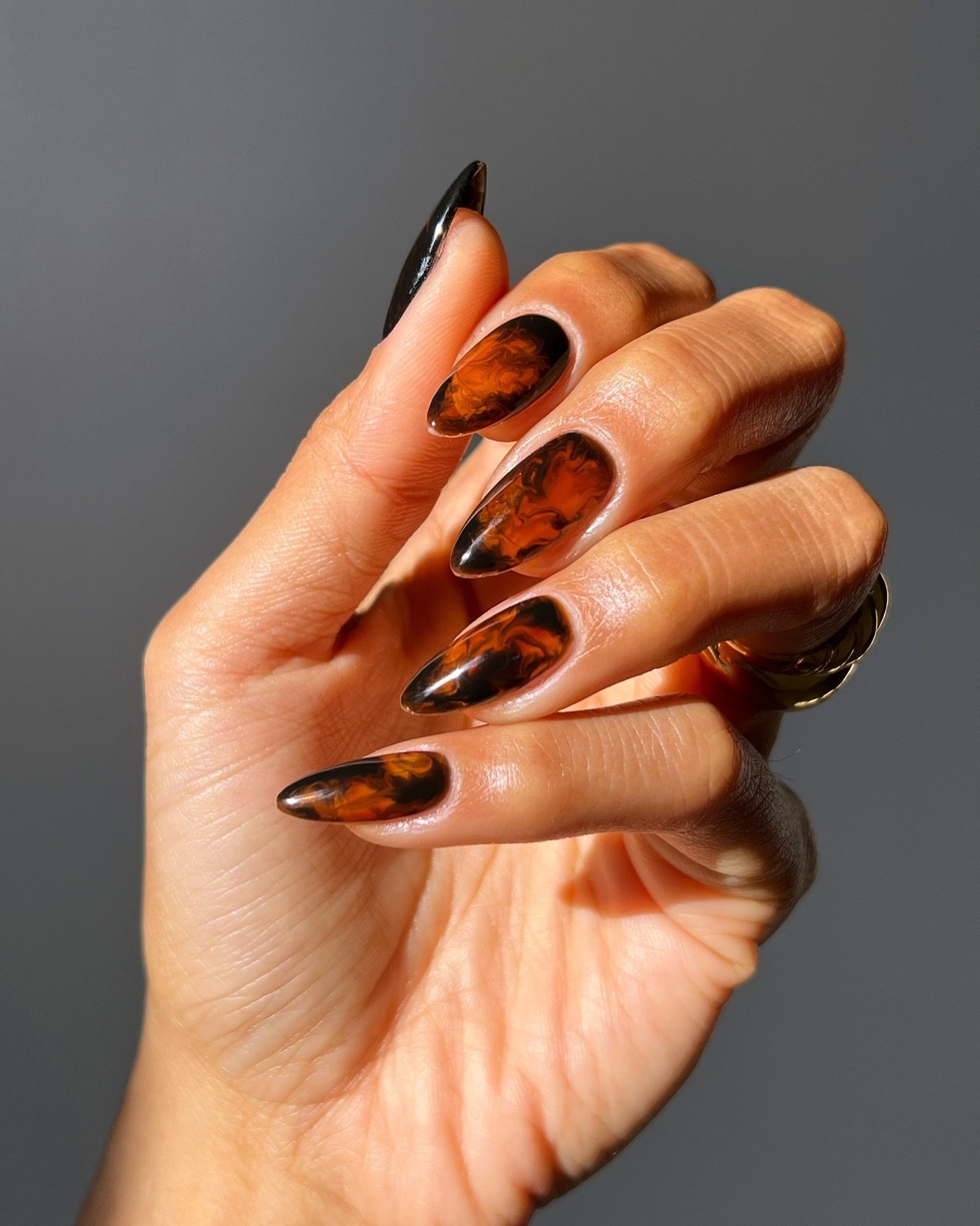 Unhas decoradas com esmalte marrom e preto, lembrando folhas de outono.