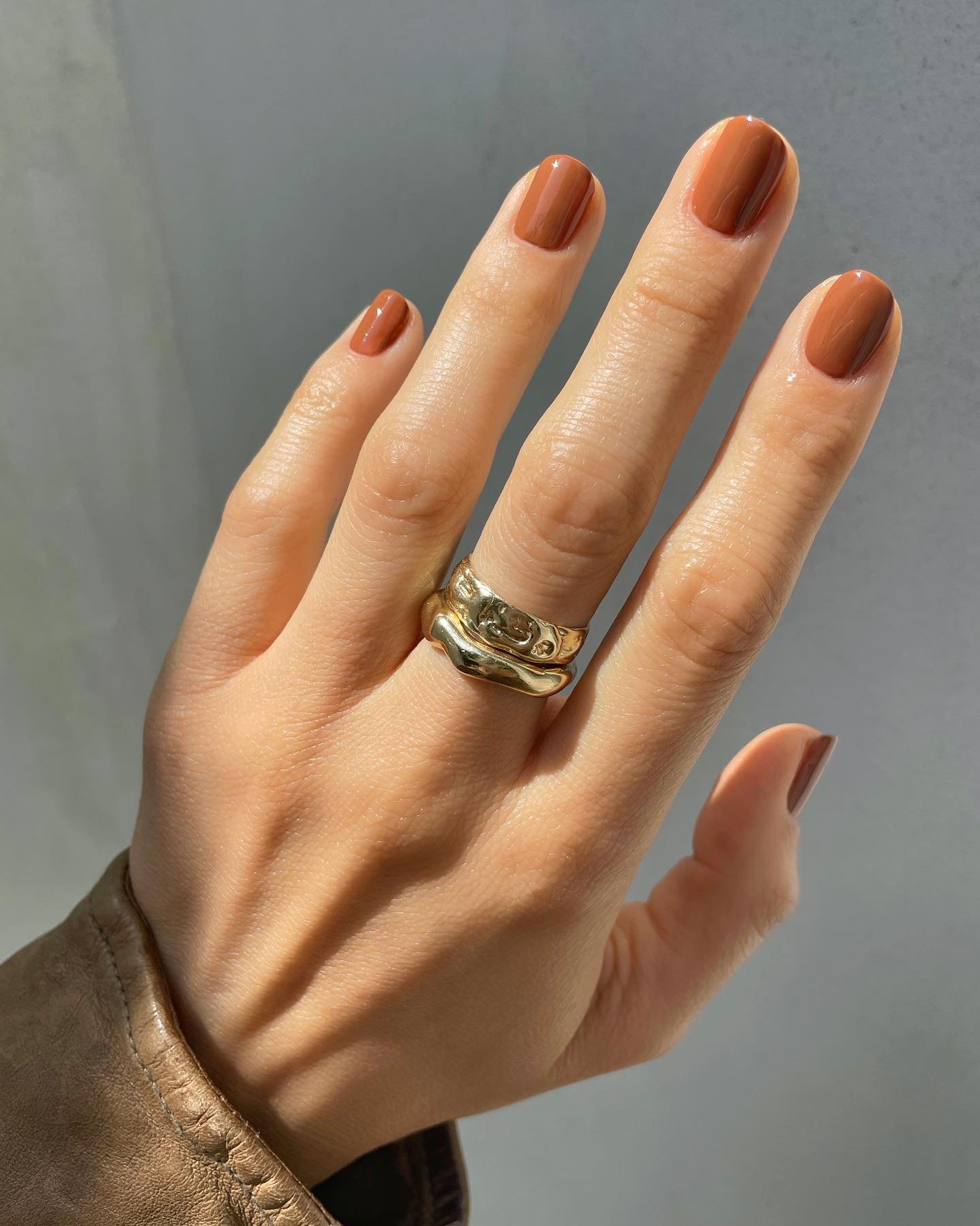 Unhas de outono em tom marrom, destacadas por anéis dourados estilizados.