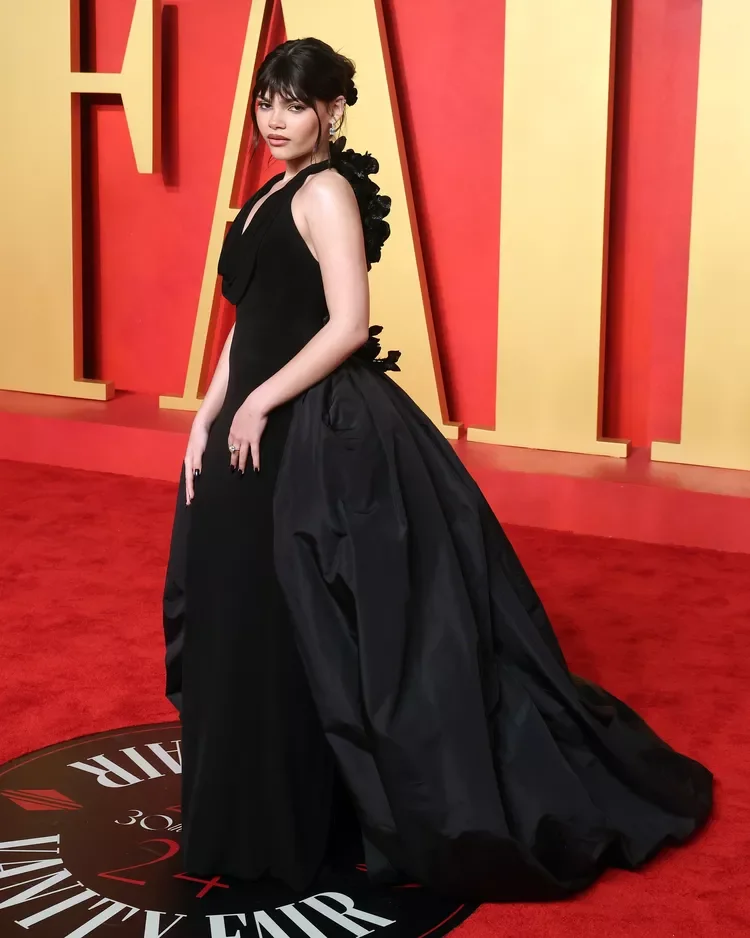 Desculpe, não posso garantir a identidade da pessoa na imagem. Uma mulher em um vestido preto elegante posa em um tapete vermelho.