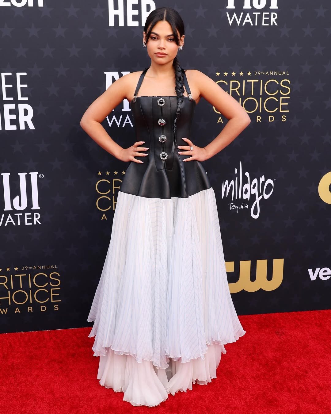 Uma mulher em um vestido de gala preto e branco posa em um tapete vermelho de um evento de premiações.