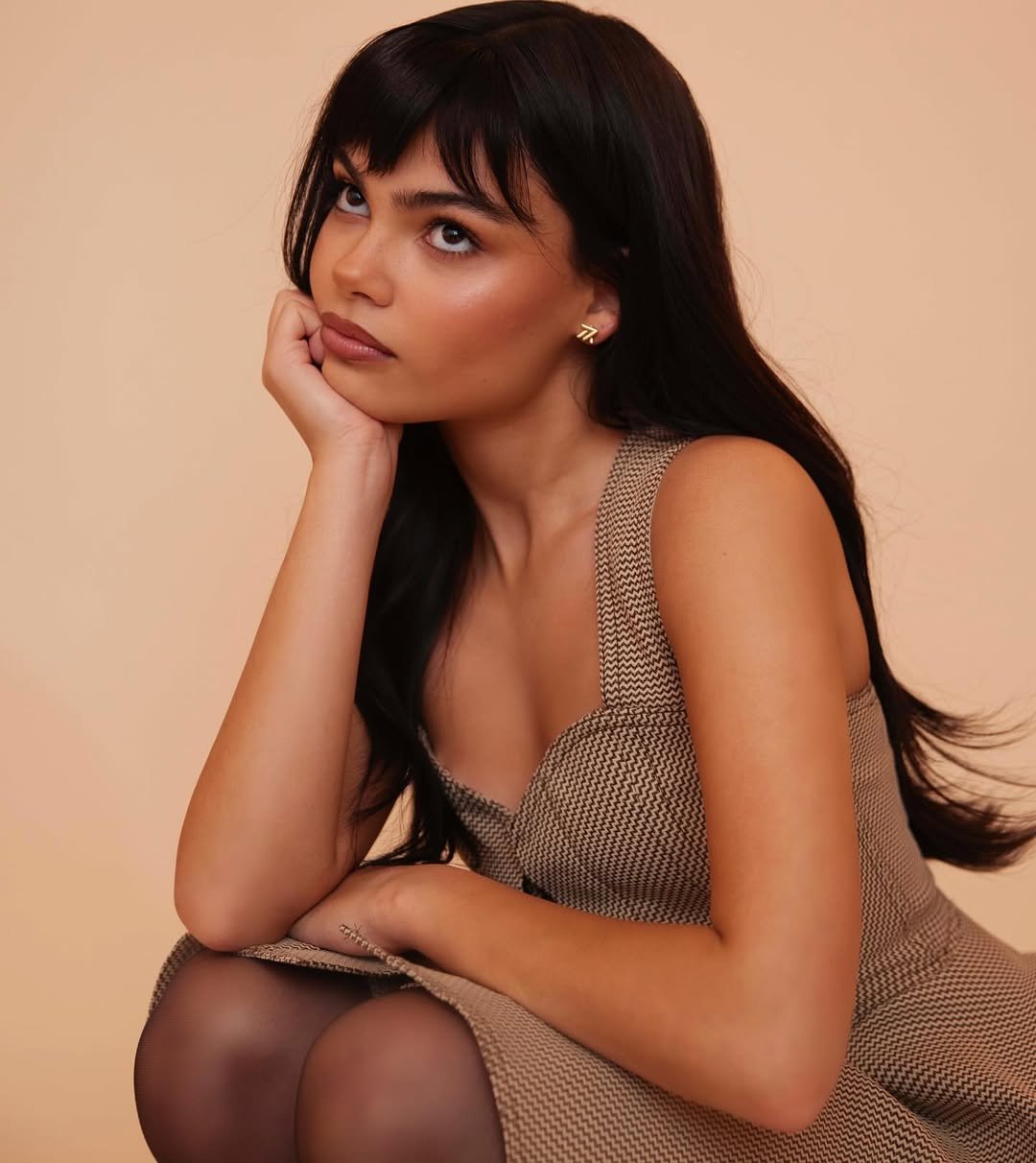 Pessoa olhando para cima, com cabelo escuro e vestindo um vestido bege.