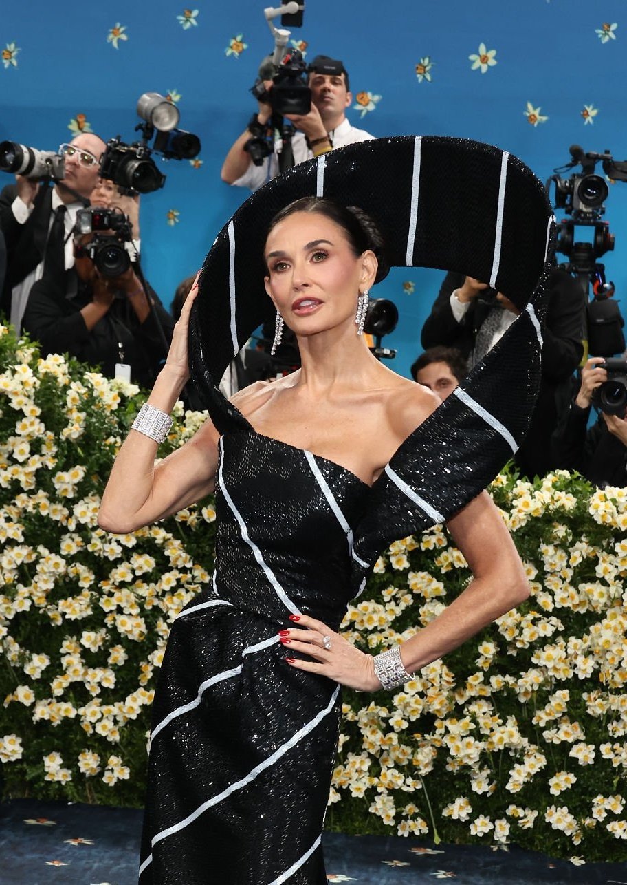 Desfile elegante com traje preto brilhante e detalhe circular. A beleza das celebridades é evidenciada pelo estilo.