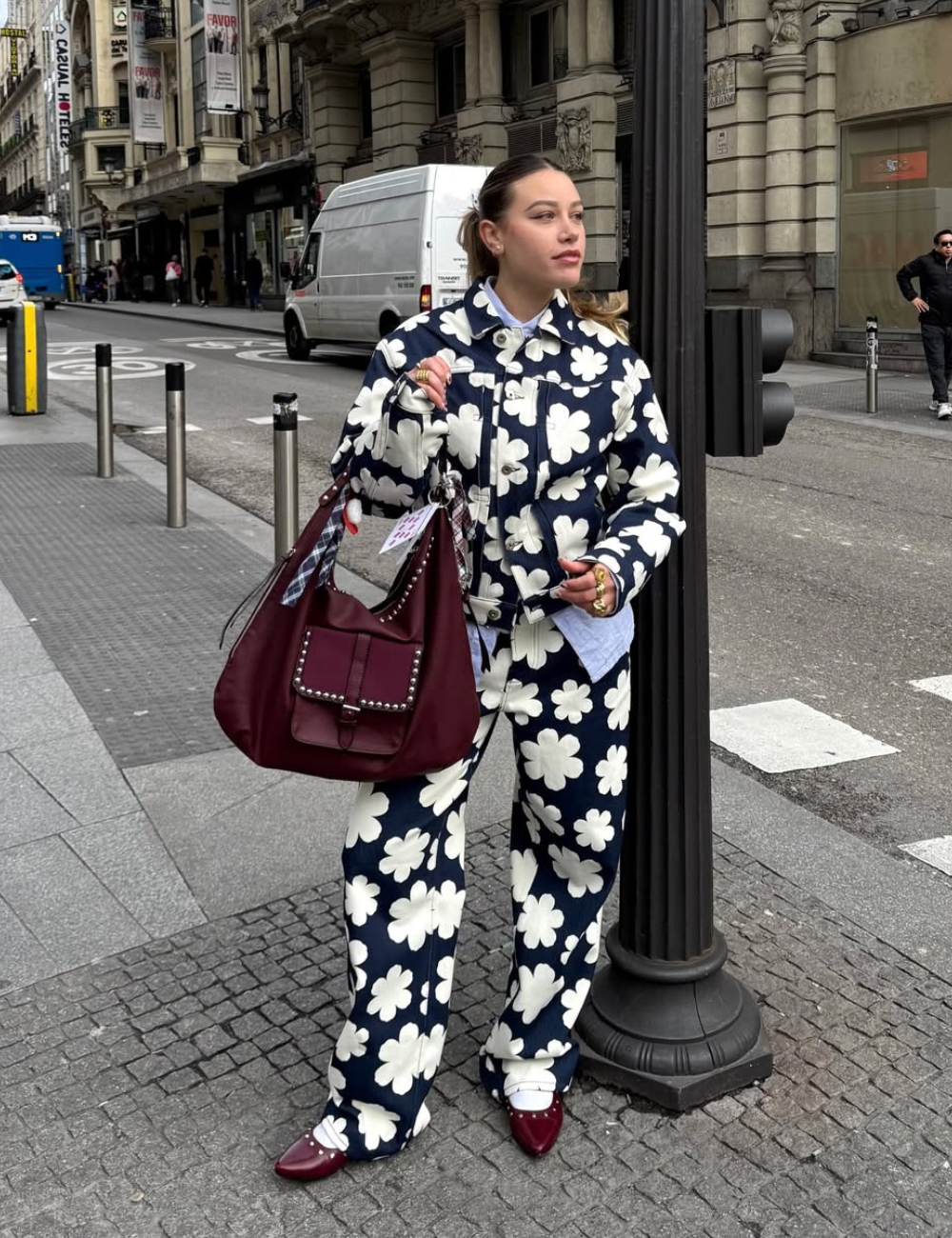 Pessoa com roupa floral azul e bolsa grande vinho, em rua movimentada urbana.