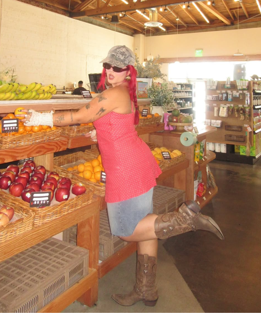Mulher de chapéu e botas de cowboy pega frutas em uma mercearia.