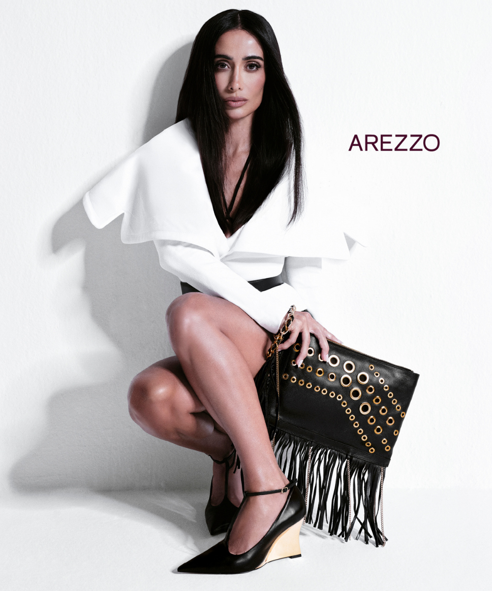 Silvia Braz usando um vestido branco elegante e bolsa preta com franjas e detalhes dourados da Arezzo.