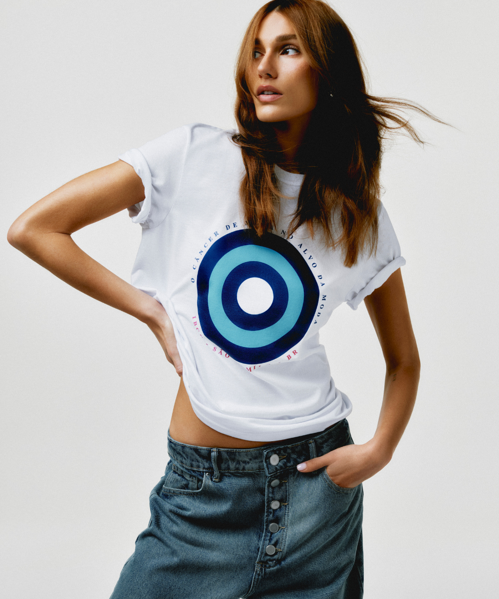 Mulher com camiseta estampada destacando círculo azul e texto sobre câncer de mama, vestindo saia jeans.