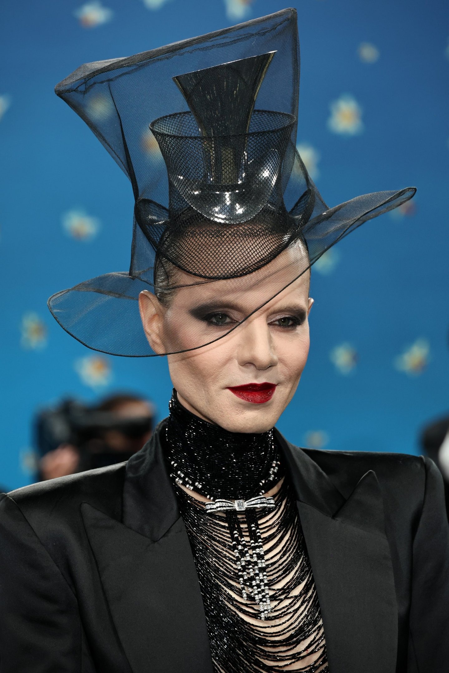 Pessoa usando chapéu futurista com véu transparente e roupa preta elegante, em um evento de moda ousado.