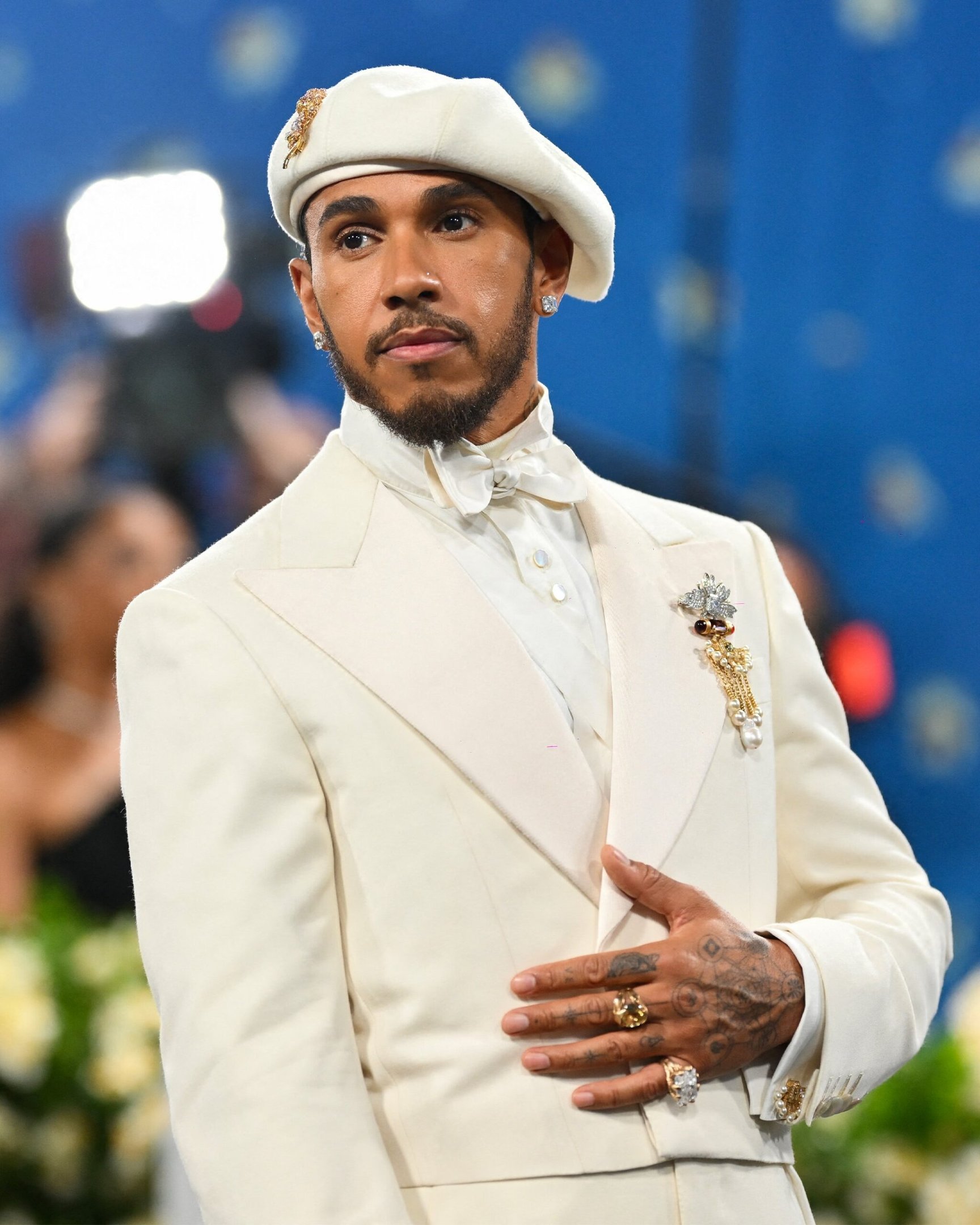 Homem em traje branco elegante com boina e broche, refletindo a tendência do Met Gala 2025.