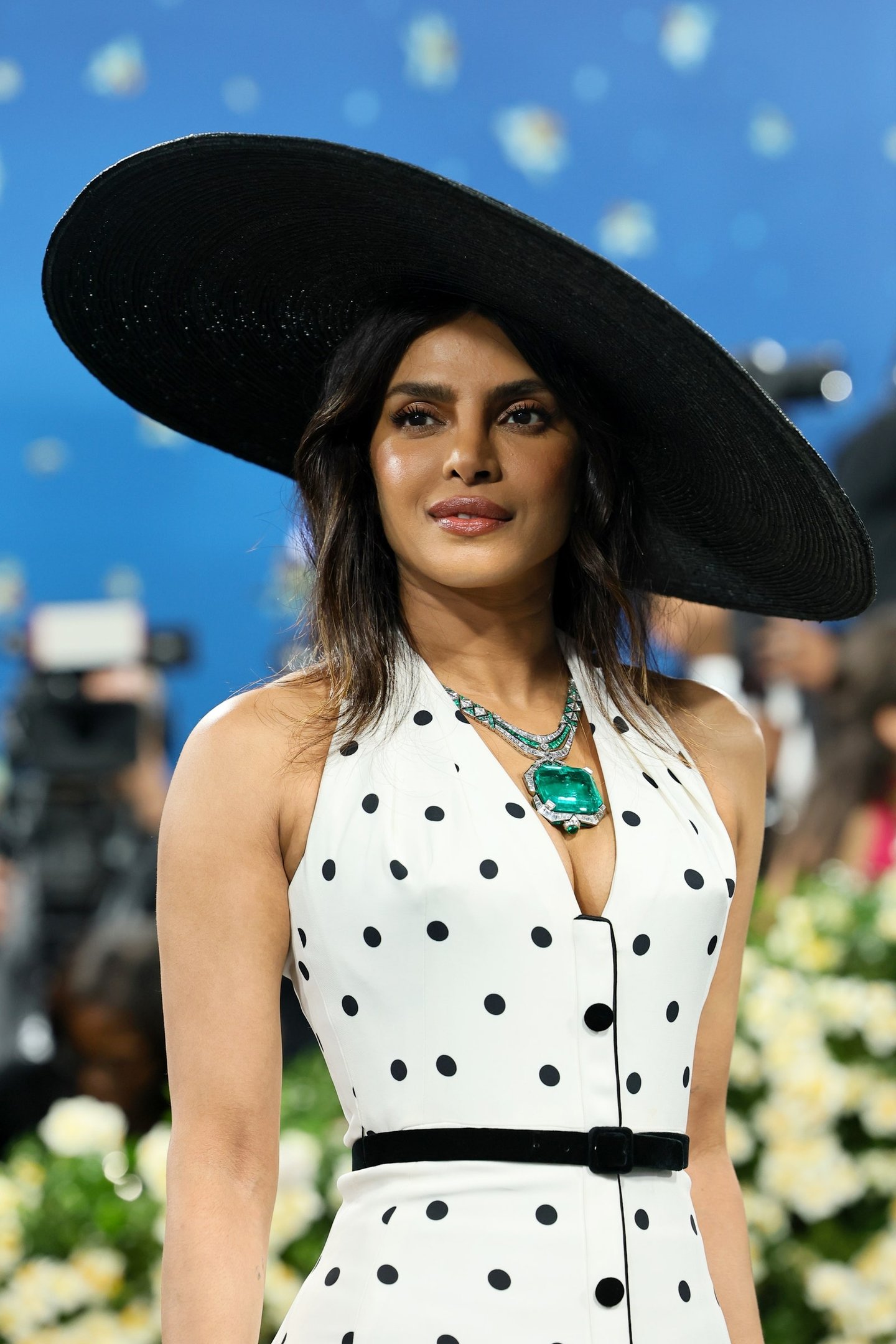 Vestido com estampa de bolinhas preto e branco, colar esmeralda e chapéu largo. Elegância em alta para o Met Gala 2025.