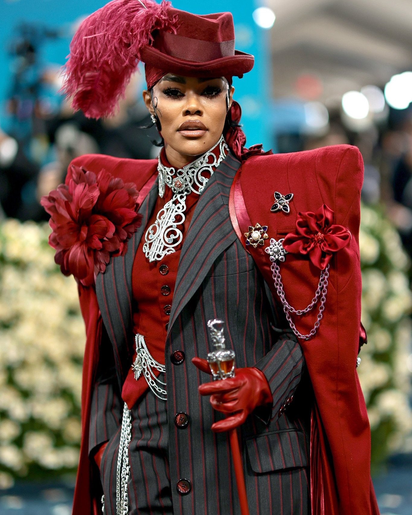 Usuário em evento de gala com traje vermelho e listras pretas. Acessórios chamativos como chapéu e luvas.