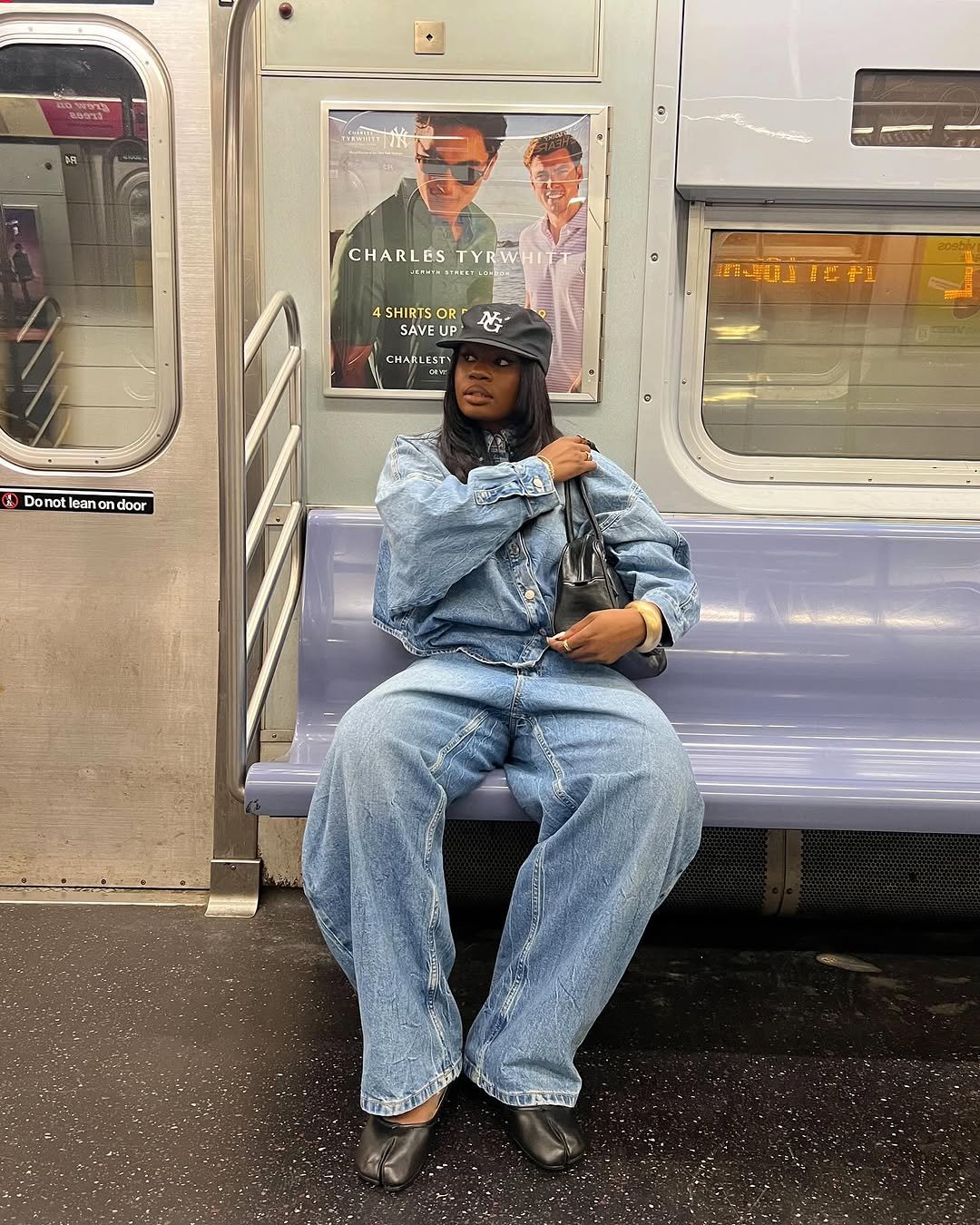 Pessoa em conjunto jeans largo e sapatilhas pretas sentada em um metrô.