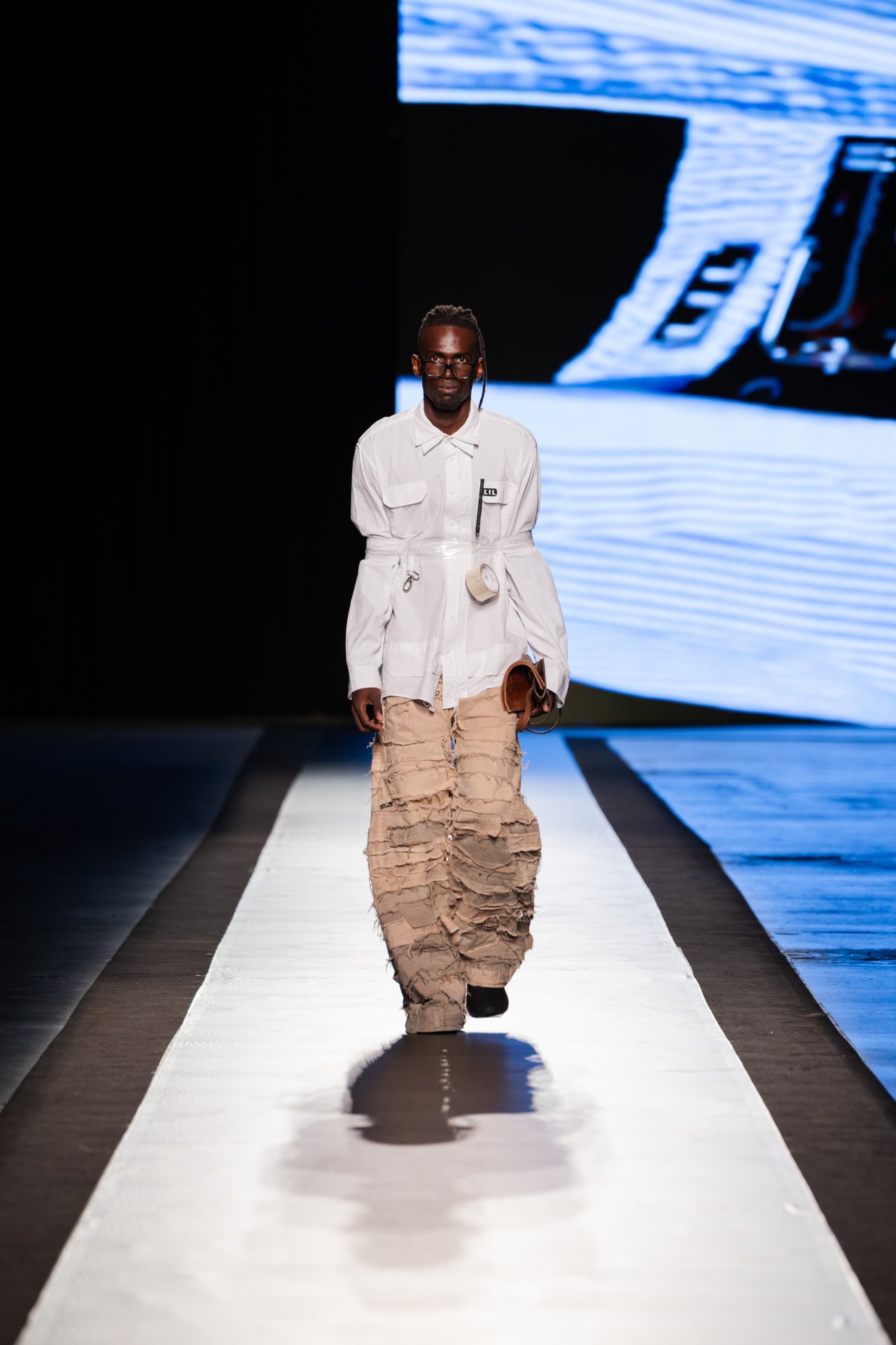 Modelo com casaco branco e calça bege texturizada em desfile do DFB Festival 2025.