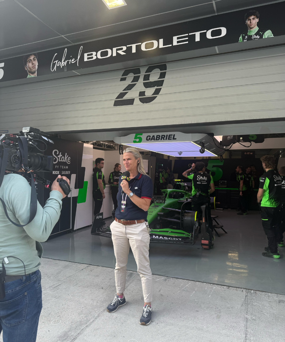 Pessoa sendo entrevistada em frente à garagem da equipe de corridas de Gabriel Bortoleto.