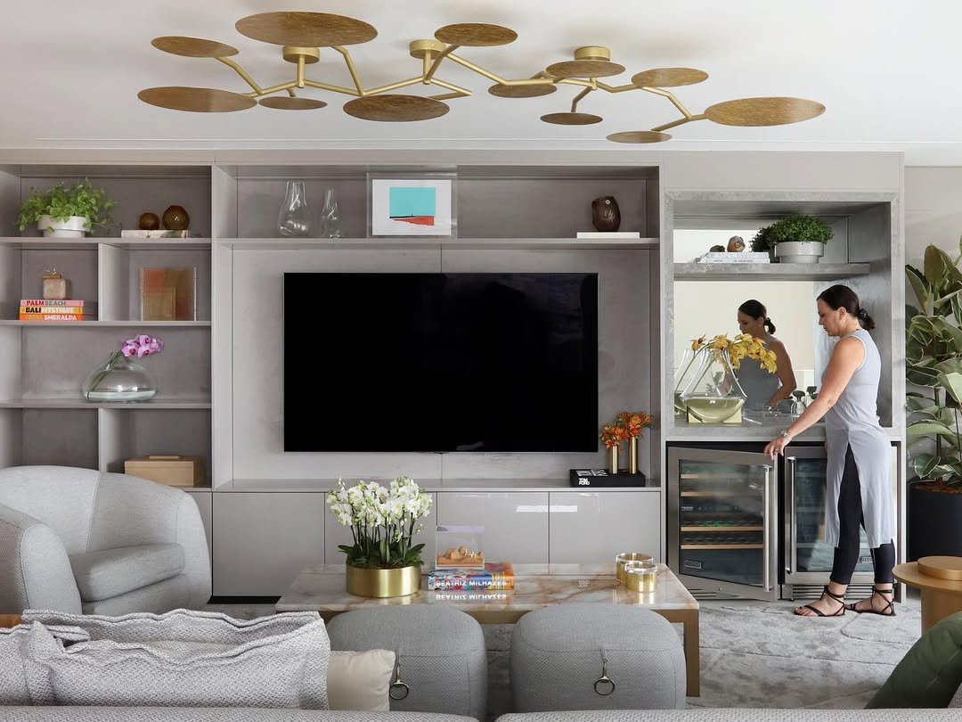 Estante na decoração, centralizando televisão e uma mulher ao lado de minibar.