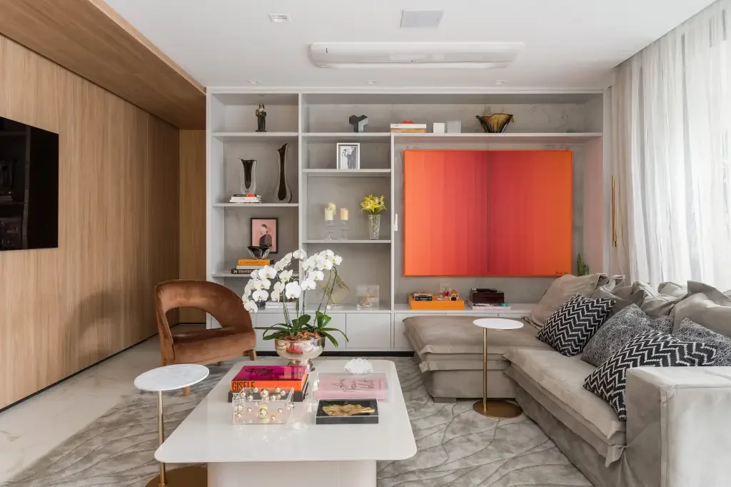 Sala de estar elegante com estante na decoração com livros e objetos de arte. Sofá e poltrona complementam o espaço.