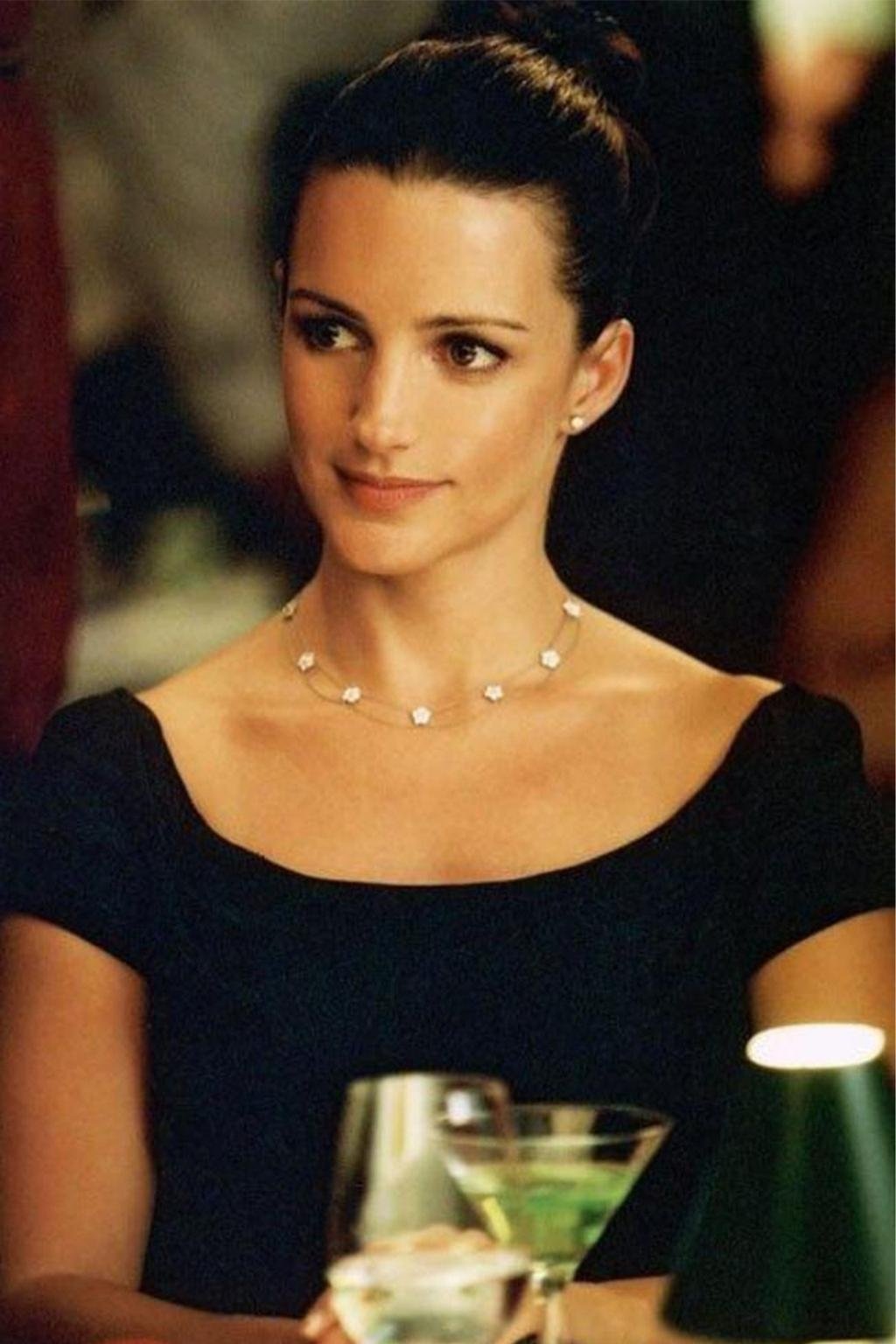 Mulher elegante de vestido preto e colar simples, com cabelo preso. Estilo clássico semelhante a Charlotte York.