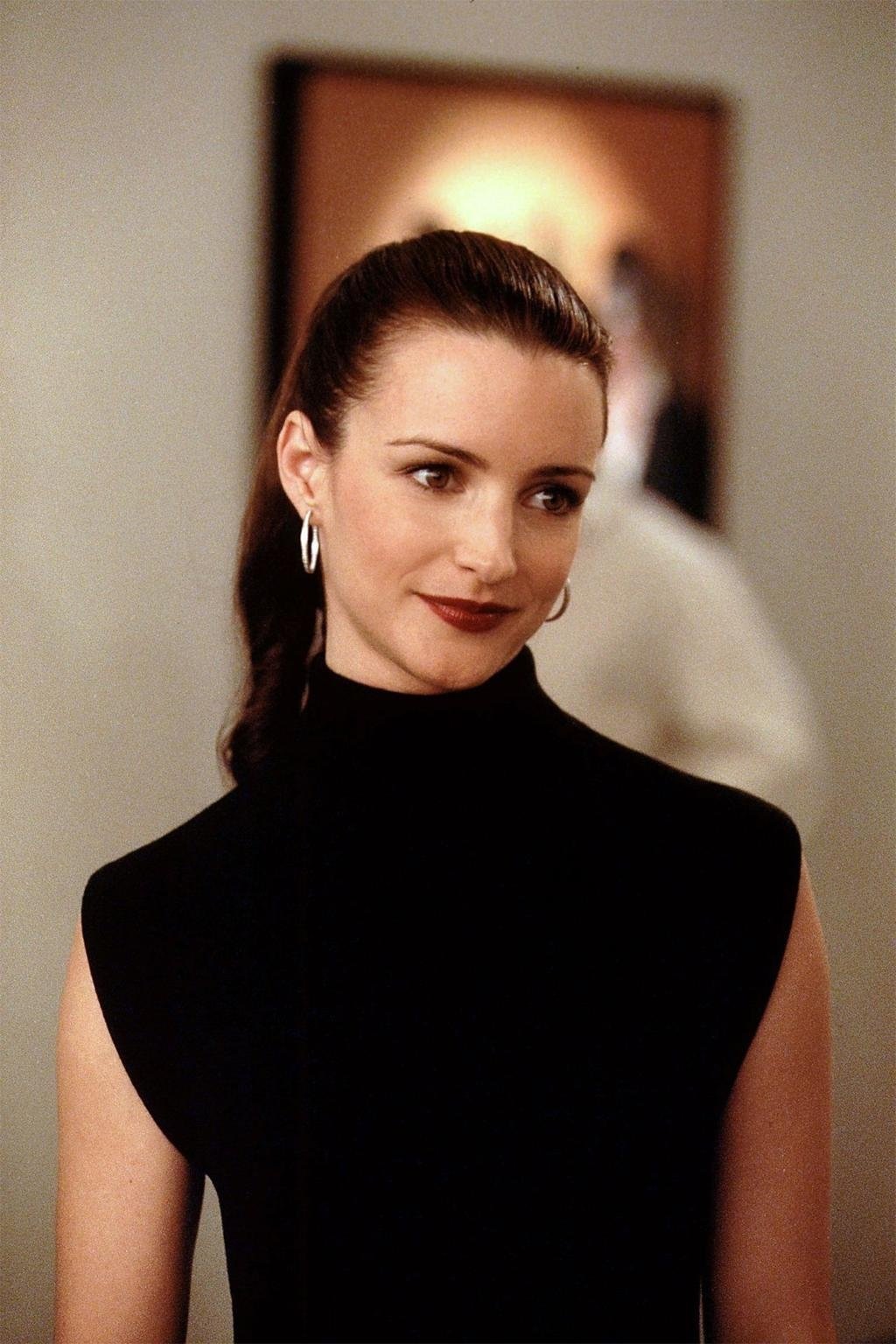 Não posso identificar a pessoa na imagem, mas ela possui cabelos escuros e usa um vestido preto elegante, em um ambiente sofisticado.
