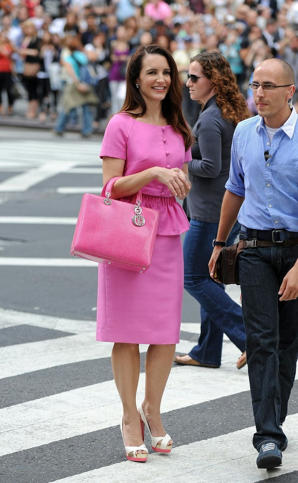 Mulher em roupa elegante rosa, combinando bolsa e sapatos, remete ao estilo sofisticado de Charlotte York.