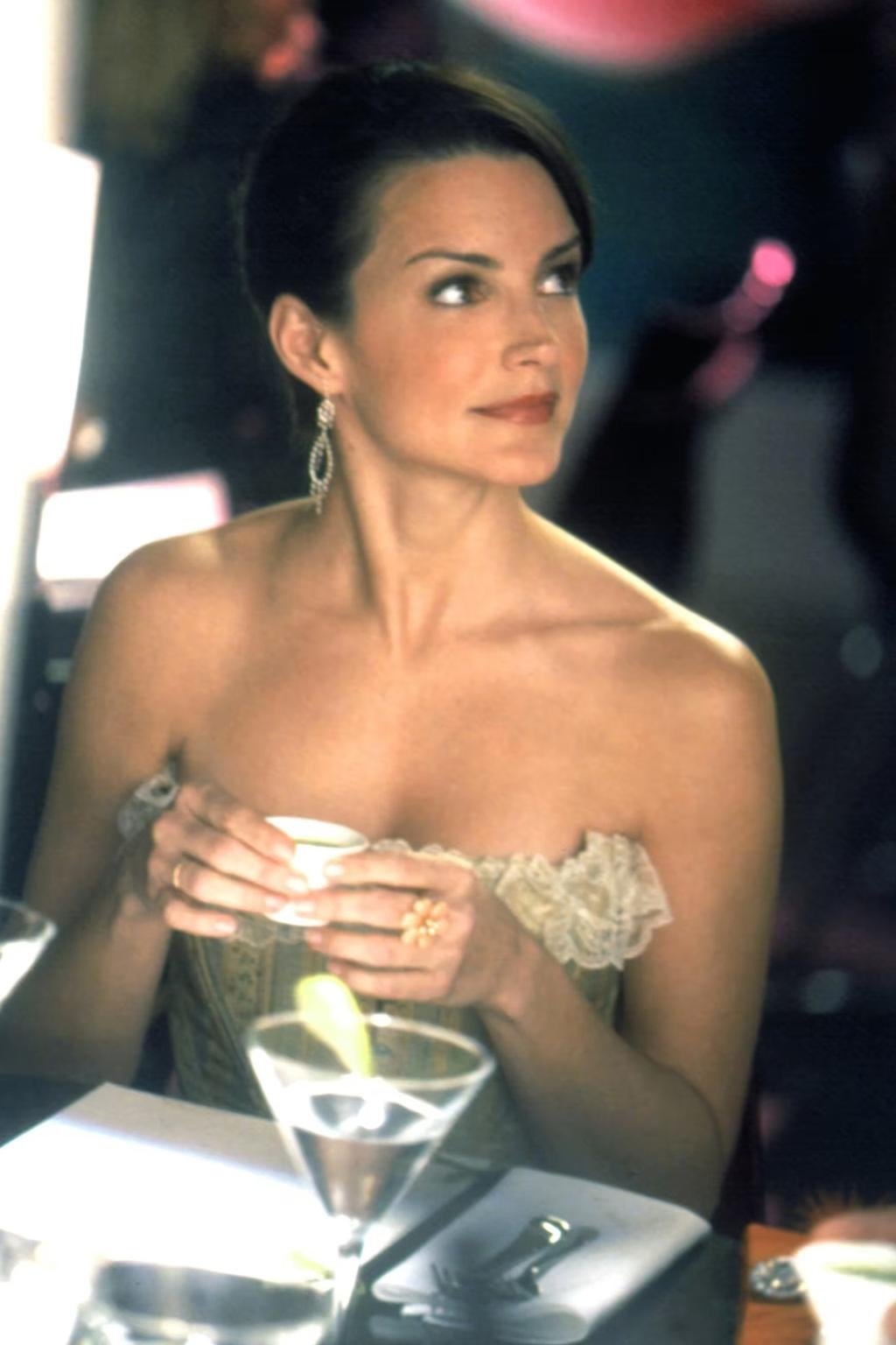 Mulher elegante segura xícara em um evento sofisticado, vestindo traje clássico e joias, lembrando o estilo de Charlotte York.