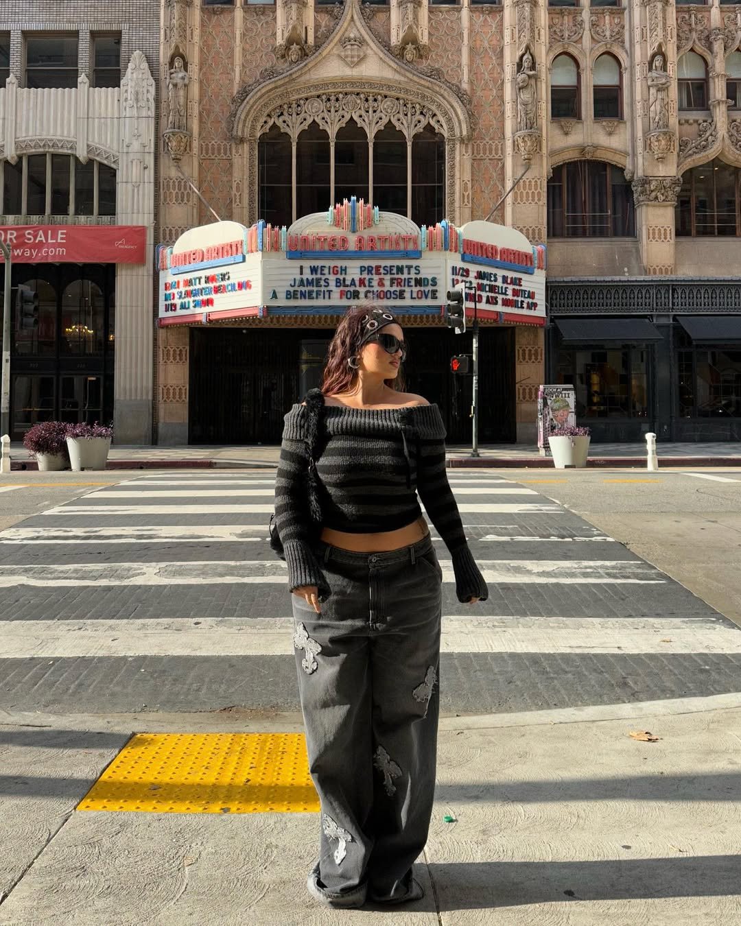 Mulher em rua de cidade, usando blusa listrada, calça jeans larga e faixa de cabelo tendência.