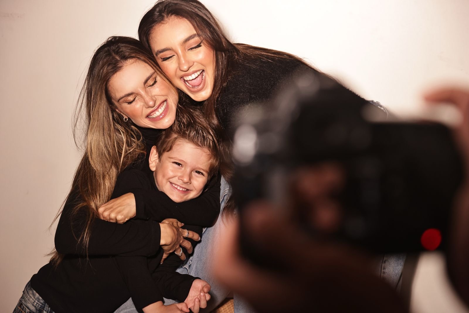 Flávia Viana e filhos sorrindo e abraçando uma criança enquanto são fotografadas.