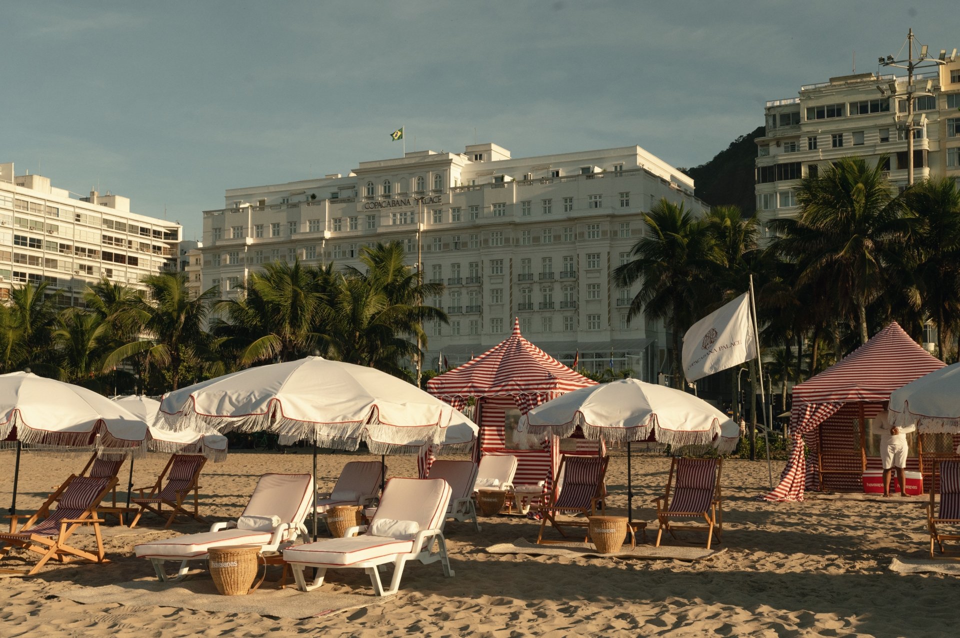 Praia com espreguiçadeiras e guarda-sóis, ao fundo o renomado Copacabana Palace.
