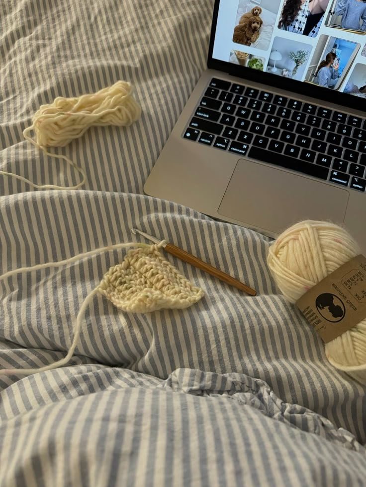 Crochê em progresso sobre coberta listrada, com fios e laptop ao lado, sugerindo hobbies manuais e inspiração online.