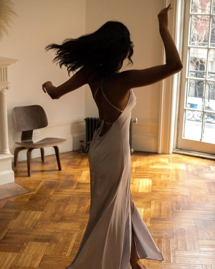 Pessoa dançando em sala iluminada com piso de madeira, vestido esvoaçante, expressando liberdade e paixão pela dança, hobbies.