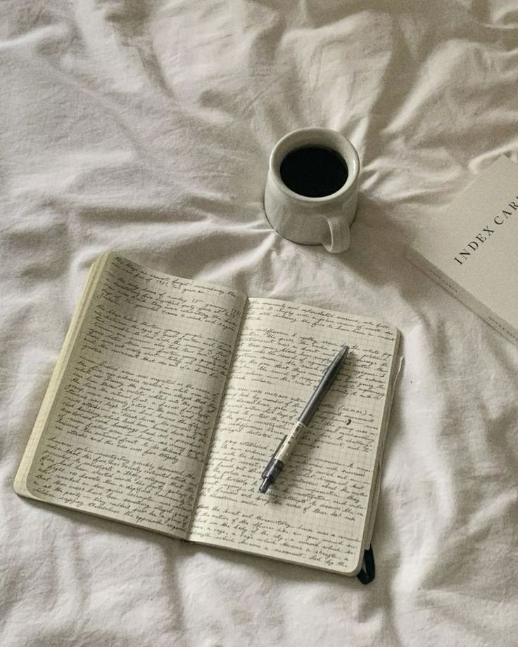 Caderno com anotações, caneta e xícara de café sobre cama, sugerindo hobbies de escrever e relaxar.