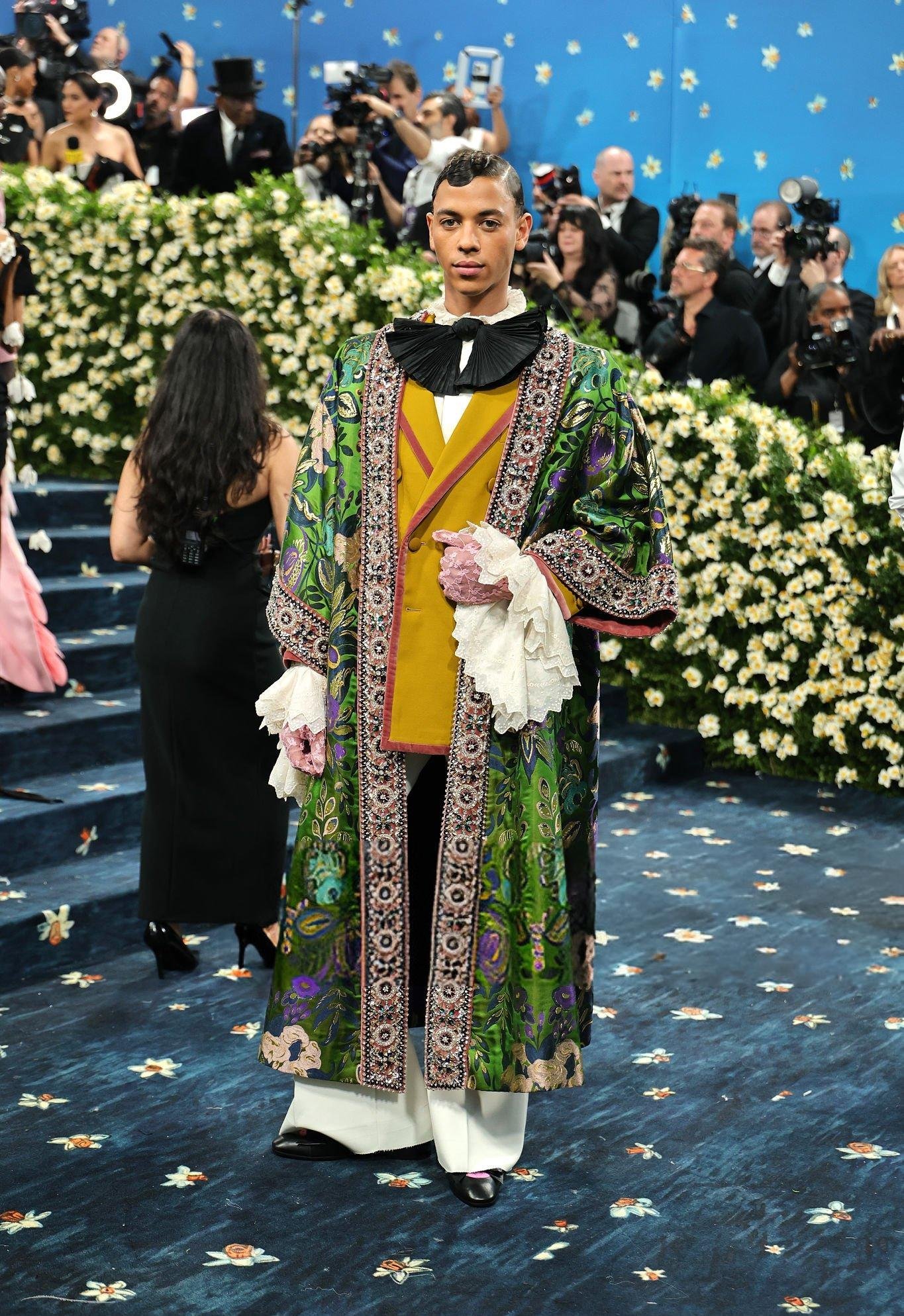 Celebridade em traje extravagante com túnica verde estampada, laces brancas e luvas rosa. Looks masculinos contemporâneos. Looks masculinos