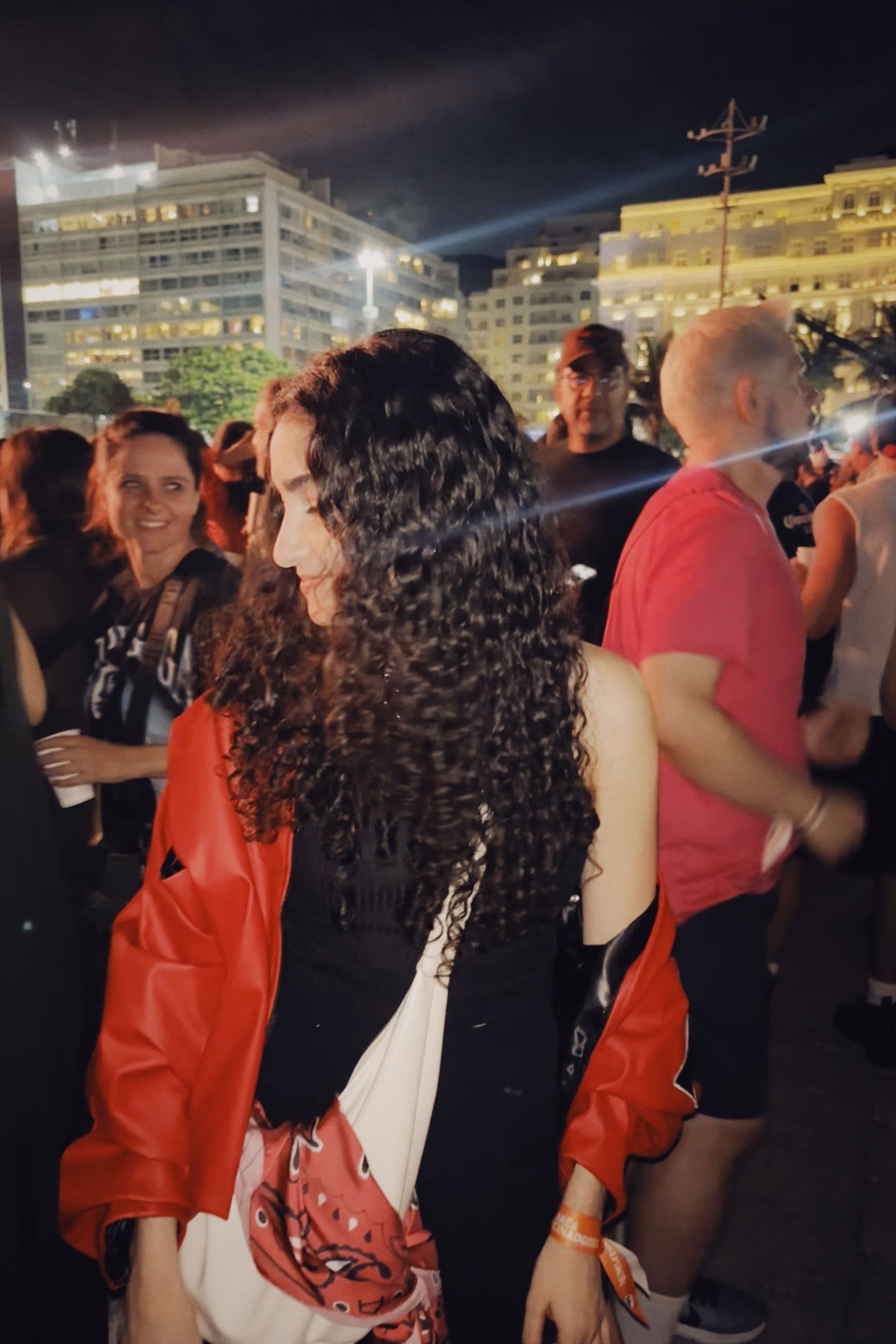Pessoas se divertindo à noite, mulher em destaque com cabelo cacheado, possível uso de leave-in antifrizz.