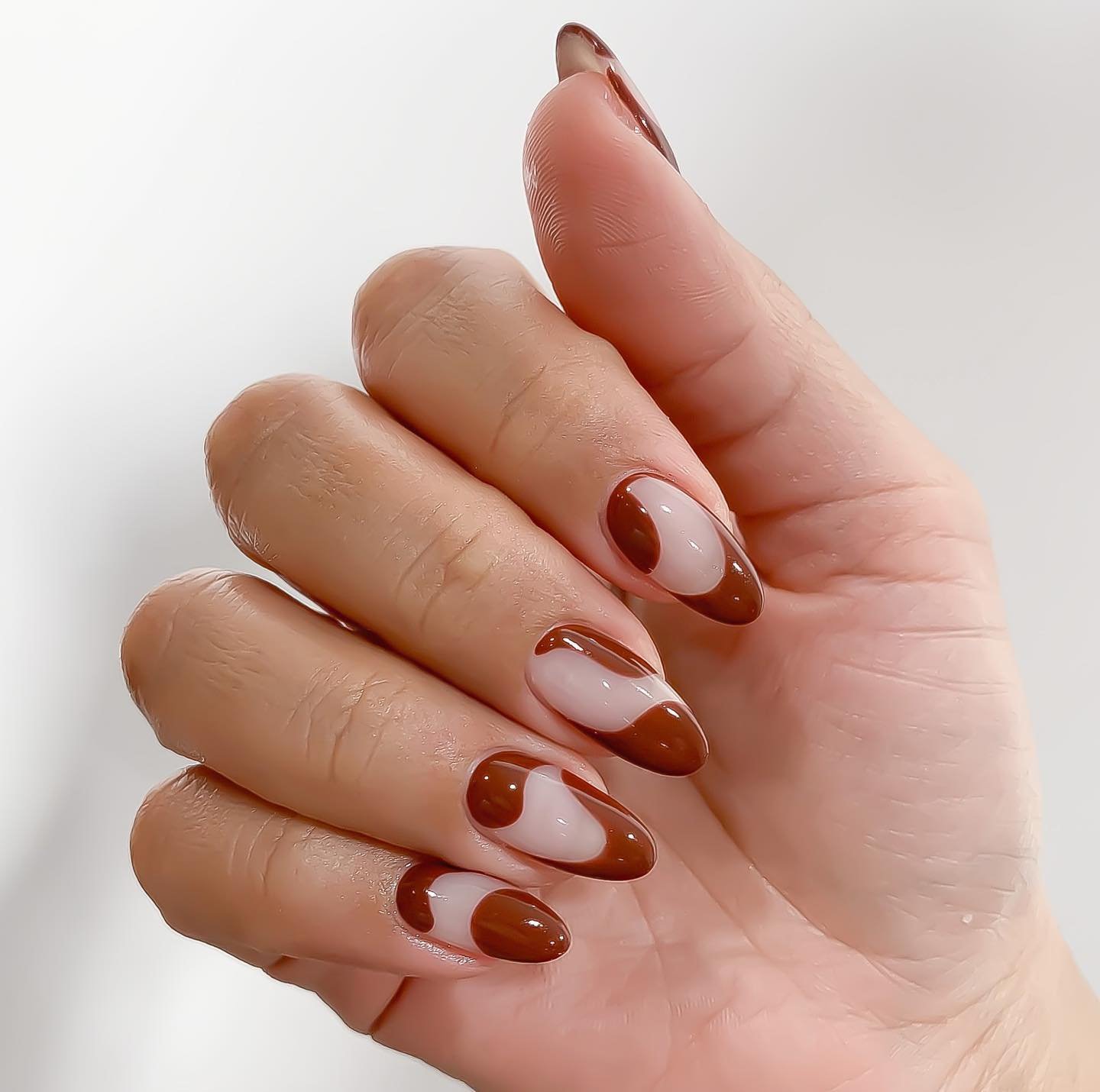 Unhas decoradas com esmalte marrom e nude em padrão geométrico elegante.