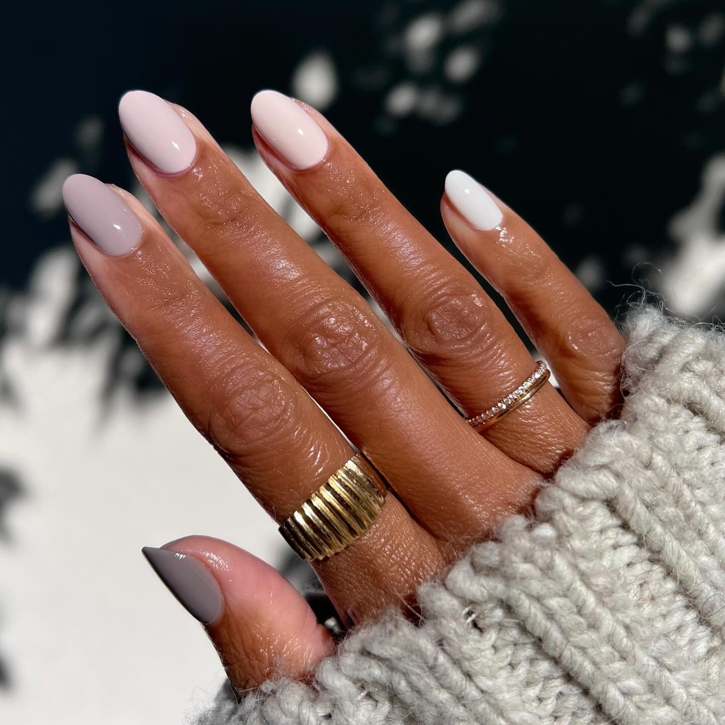 Mão com unhas de gel em tons neutros suaves, simples e elegantes, usando anéis dourados e prateados.