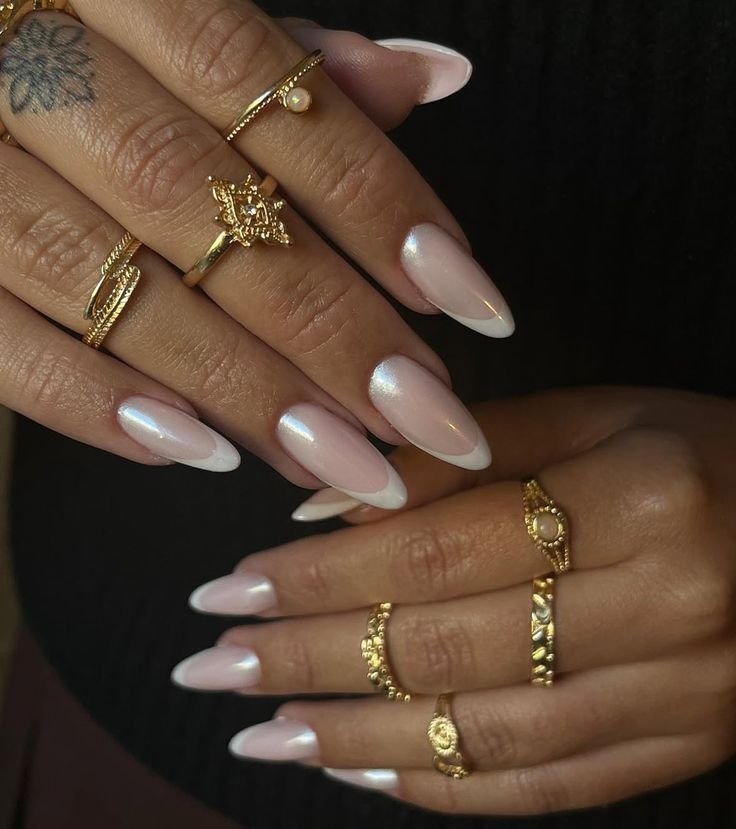 Mãos com unhas de gel simples e elegantes, estilo francesinha. Acessórios dourados adornam os dedos, destacando o brilho discreto do esmalte.