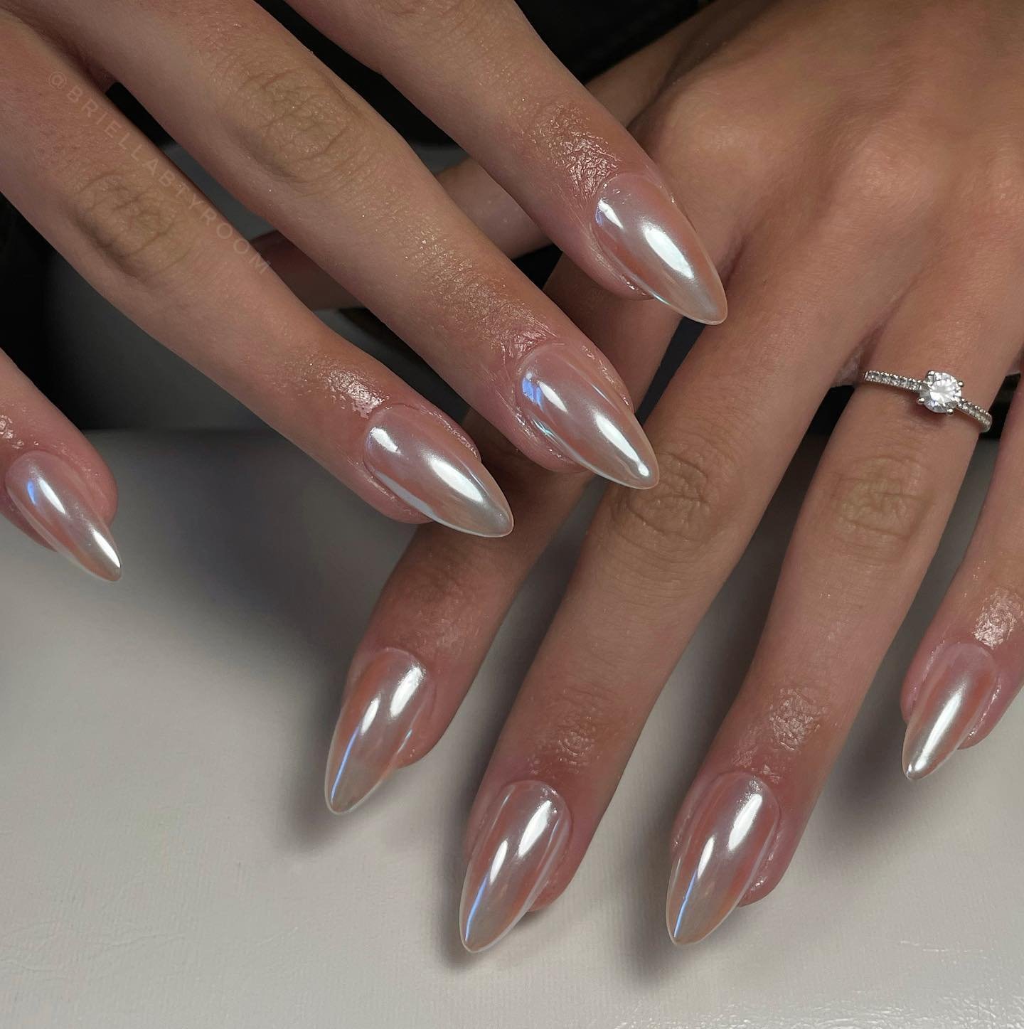 Unhas em formato amendoado com esmalte perolado, acompanhadas de anel delicado.