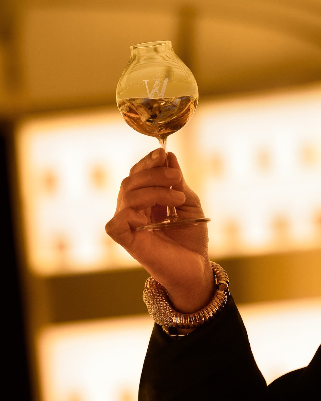 Mão feminina elegante segura uma taça com whisky, destacando a grife Johnnie Walker.