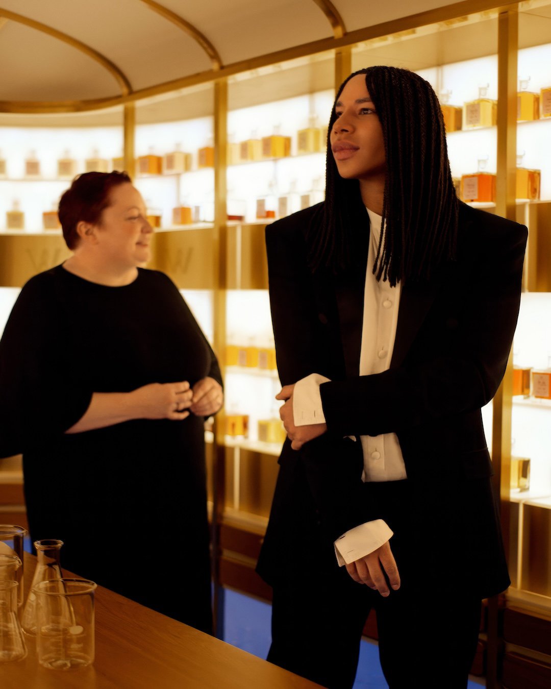 Duas pessoas em um ambiente luxuoso com várias garrafas iluminadas ao fundo, evocando o universo Johnnie Walker.