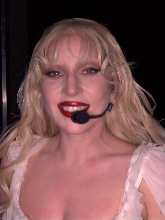 Pessoa de cabelo loiro e batom vermelho se apresentando com microfone de cabeça. Batom da Lady Gaga