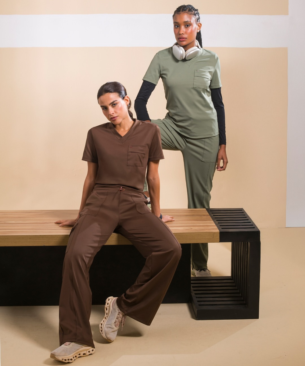 Duas pessoas em roupas marrom e verde da Linha Wellness posam em um ambiente moderno.